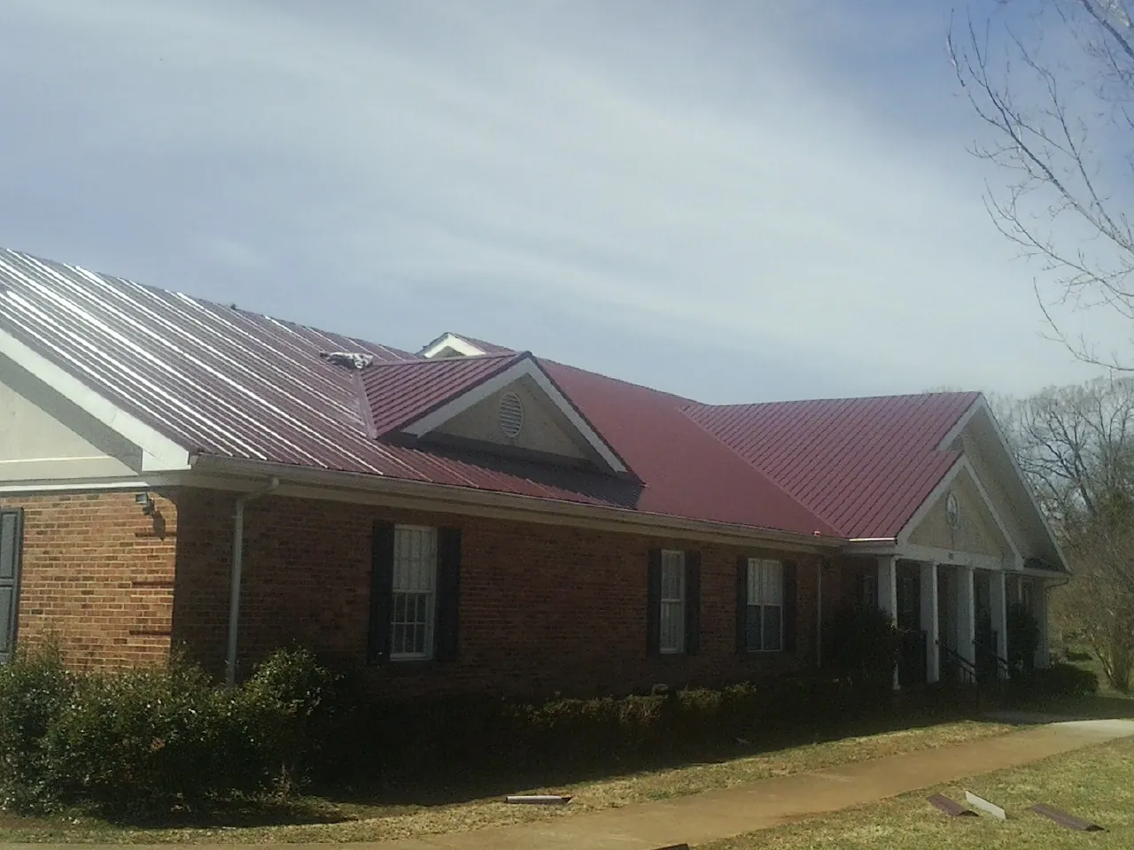 Red metal roof with gabled entries on a long brick building, from a Hail Damage Roof Repair job in Palos Hills