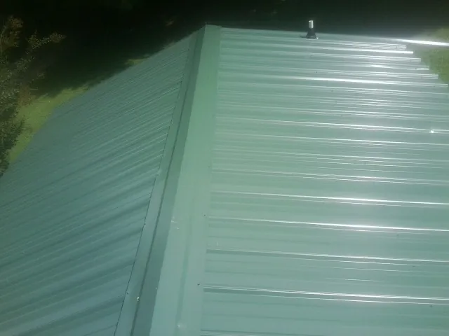 New green metal panels meeting at the ridge of a roof — Flat Roof Repair work by our crew in Palos Hills