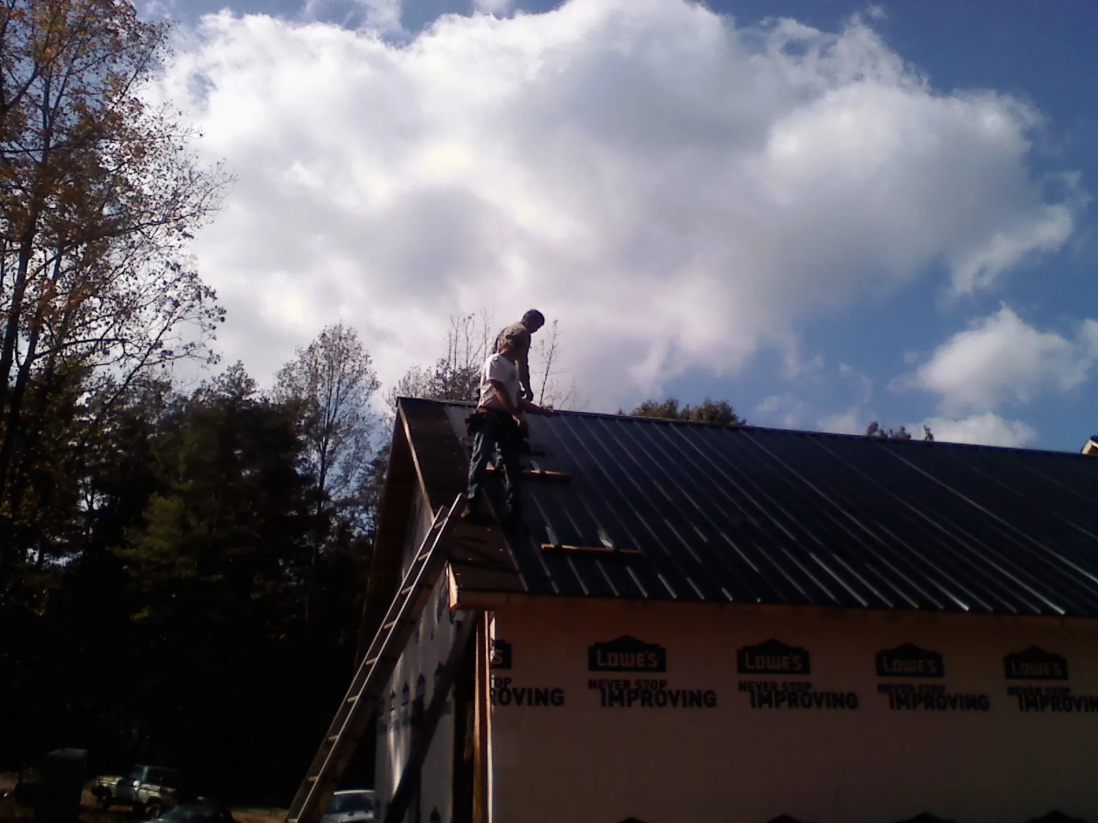 Roofer fastening dark metal panels high against a cloudy sky, from a Roof Inspection job in Palos Hills