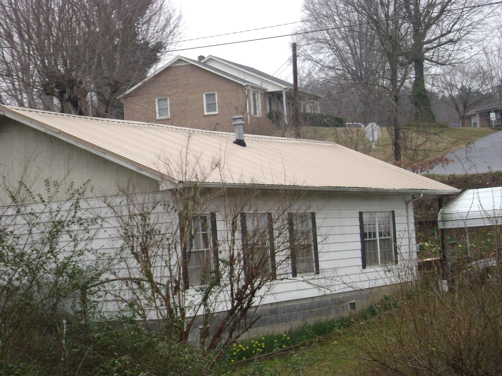 Tan metal roof on a white sided house set into a hillside — Commercial Roofing by Roofing Brothers in Palos Hills